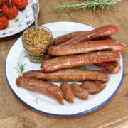cooked sausages served on a plate with a jar of mustard