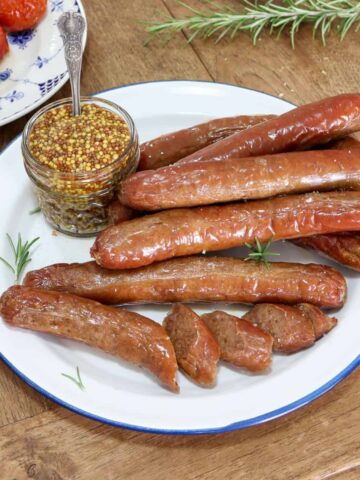 cooked sausages served on a plate with a jar of mustard