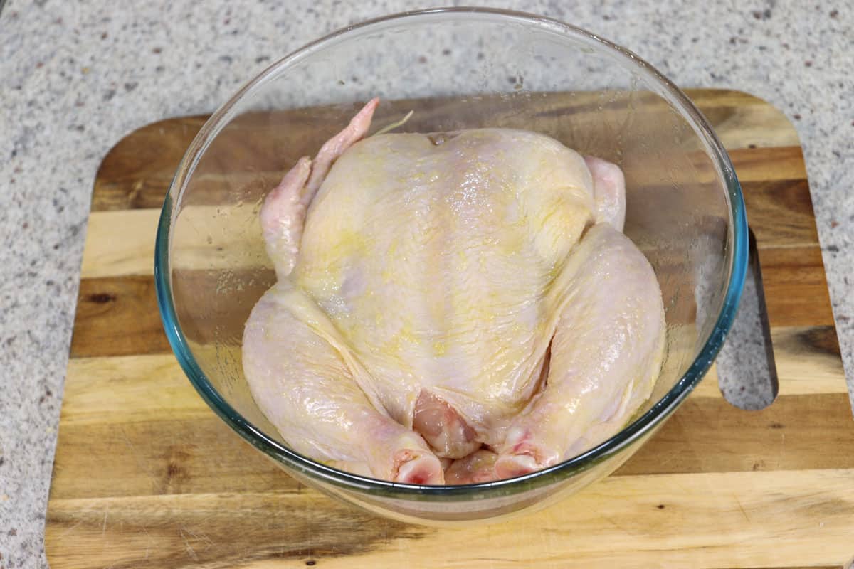 A whole chicken in a bowl coated with oil and salt