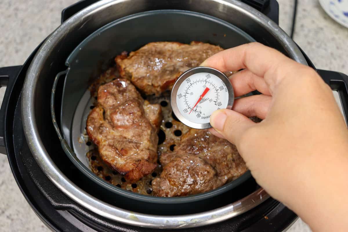 Checking the internal temperature of the pork steaks in the air fryer with a thermometer