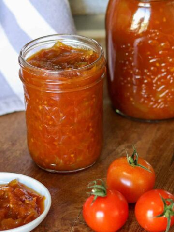 Jars of tomato relish next to raw tomatoes and a dish of tomato relish