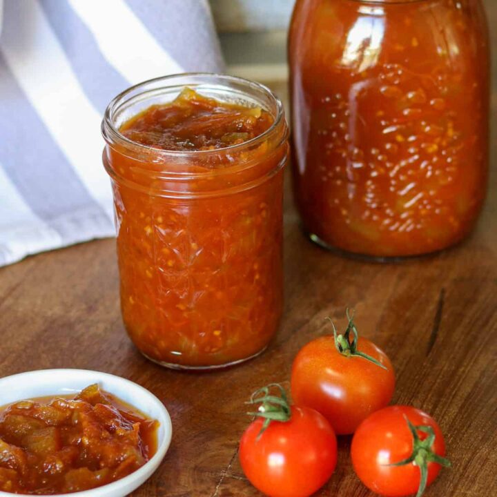 Jars of tomato relish next to raw tomatoes and a dish of tomato relish