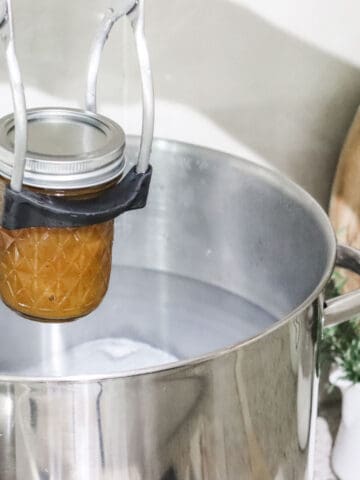 a jar filled with preserve being lowered into a water bath canner