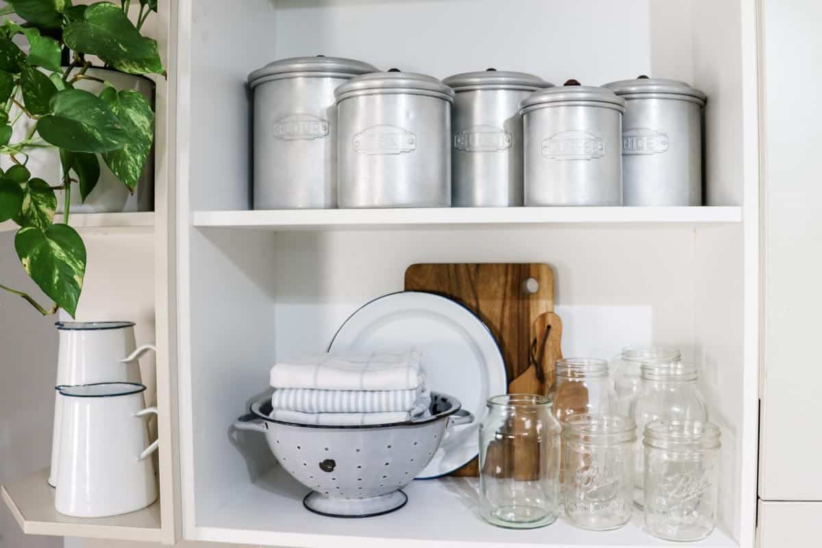 open kitchen shelving styled with canisters, an indoor plant, enamelware and various kitchen utensils