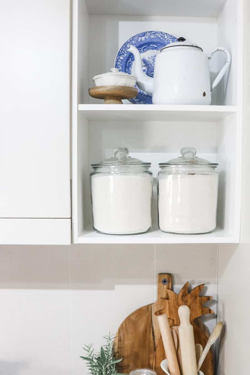 Open kitchen shelving next to a cabinet styled with a decorative plate, teapot and ingredient canisters