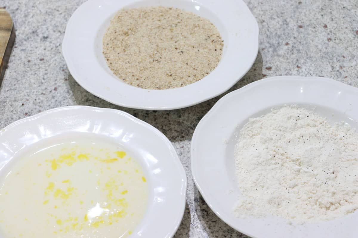 Three dishes sit on the kitchen bench, one filled with flour seasoned with salt and pepper, one with egg and milk mixture and the other with breadcrumbs, ready to crumb lamb cutlets