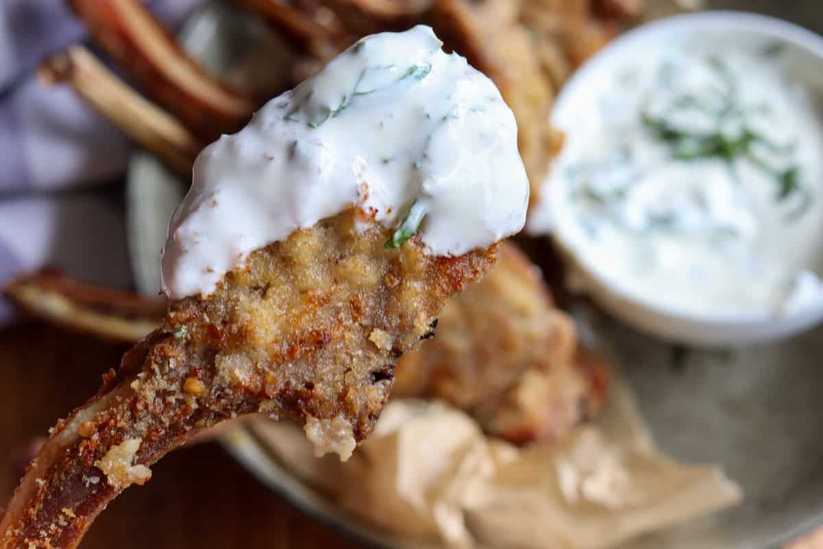 A cooked crumbed lamb cutlet dipped in yogurt and mint sauce