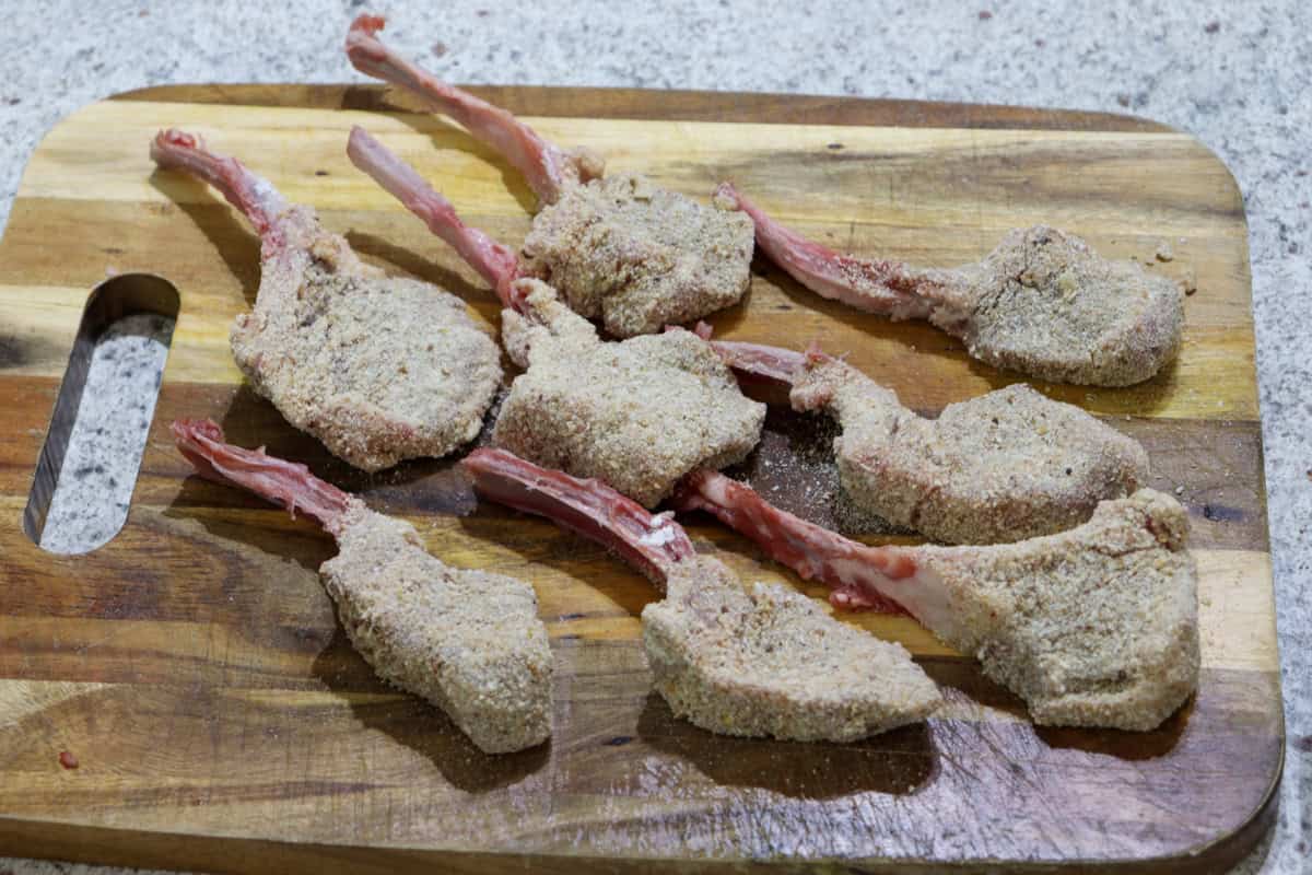 Freshly crumbed, raw lamb cutlets sit on a wooden chopping board
