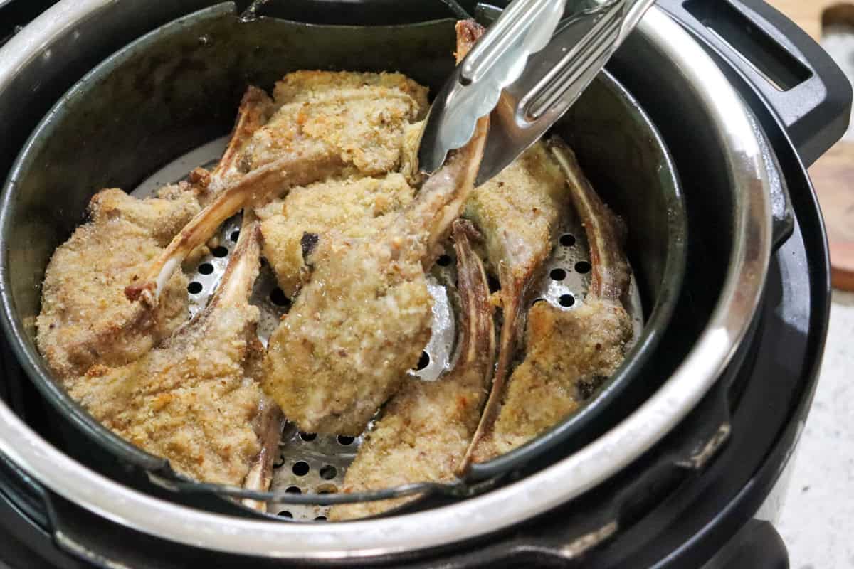 Tongs are used to flip the crumbed lamb cutlets in the air fryer basket half way through cooking