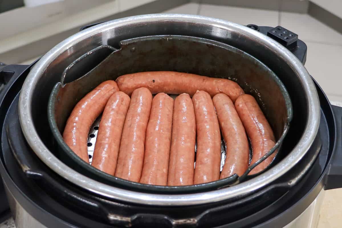 raw sausages are placed on the broiling tray in the air fryer basket
