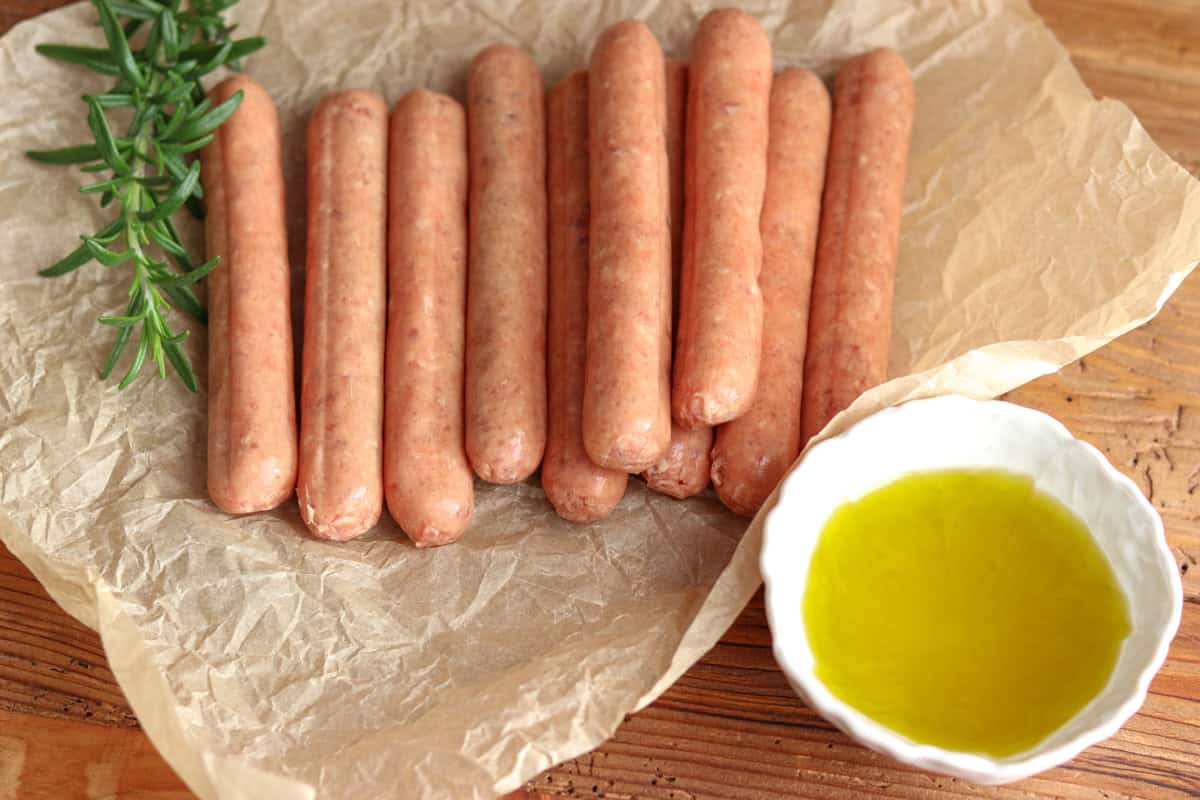 raw sausages, rosemary and a small bowl of extra virgin olive oil