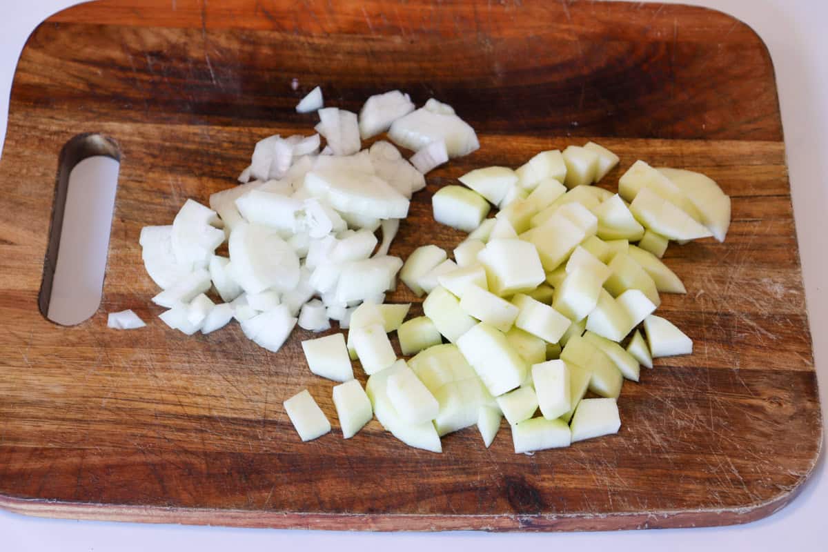 Onion and apple are diced on a wooden chopping board