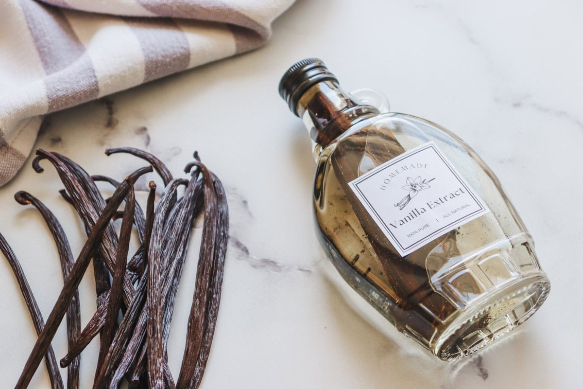A bottle of freshly made pure homemade vanilla extract on a marble surface set next to a handful of dried vanilla beans