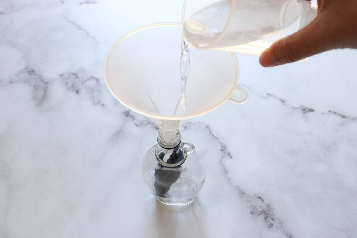 Vodka is poured from the measuring cup into the bottle using a funnel