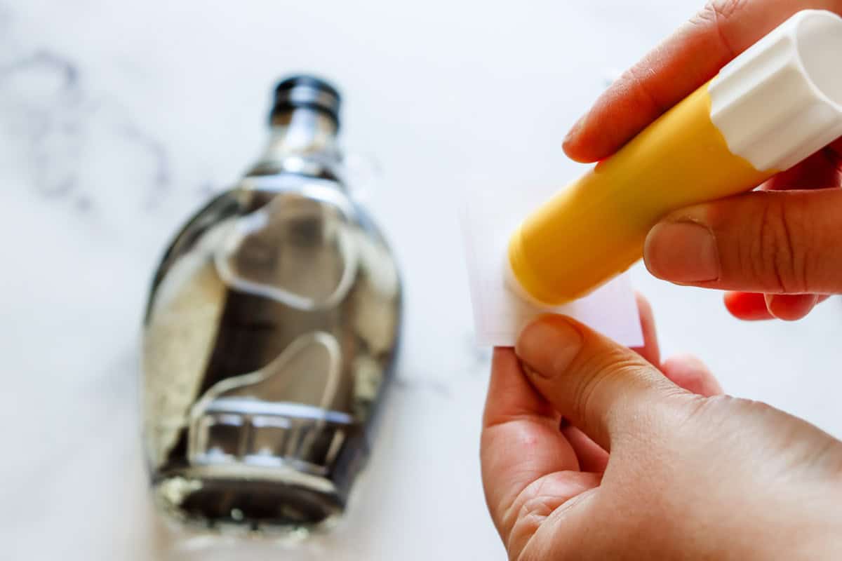A glue stick is used to transfer glue onto the label for the bottle
