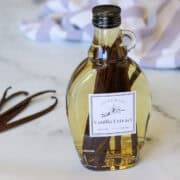 A bottle of freshly made pure homemade vanilla extract on a marble surface set next to a handful of dried vanilla beans