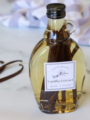 A bottle of freshly made pure homemade vanilla extract on a marble surface set next to a handful of dried vanilla beans