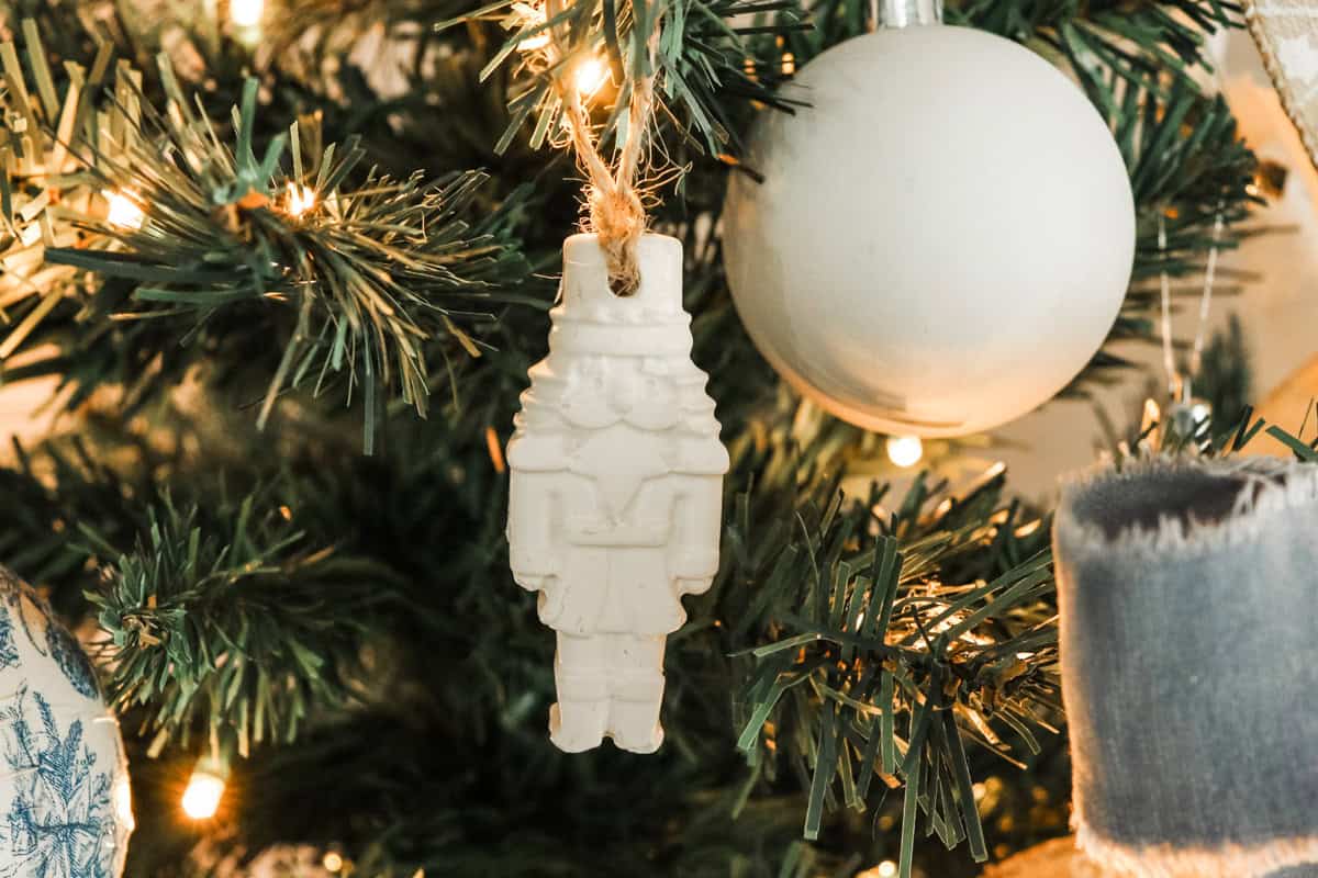 Air dry clay white nutcracker shaped Christmas ornament handing on a Christmas tree next to other ornaments