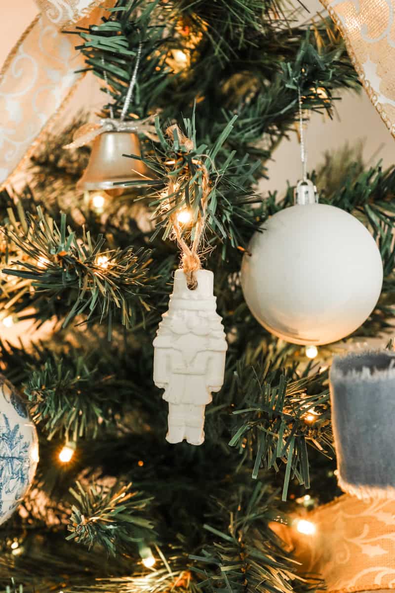 Air dry clay white nutcracker shaped Christmas ornament handing on a Christmas tree next to other ornaments
