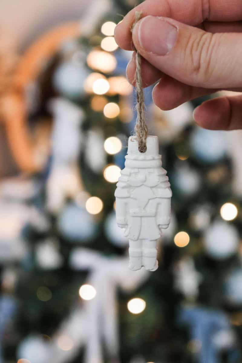 an air dry clay ornament is held by the twine by the maker in front of the Christmas tree