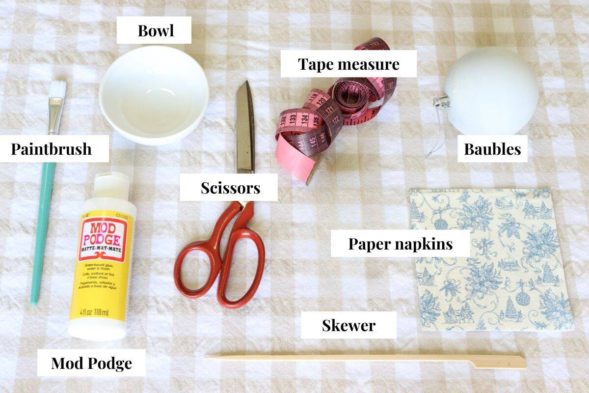 A graphic with the materials required for the project and text labels including paintbrush, bowl, Mod Podge, scissors, tape measure, baubles, paper napkins and skewer