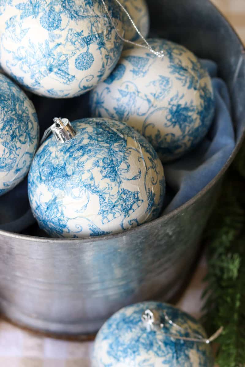Close up image of DIY blue and white paper napkin decoupage Christmas ornaments stacked in a silver bucket