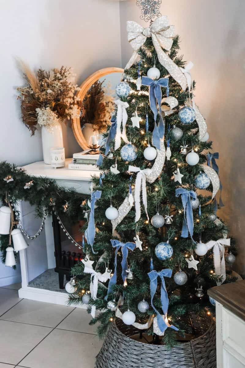 A blue and white themed Christmas tree with decoupage Christmas ornaments set infant of a fire place