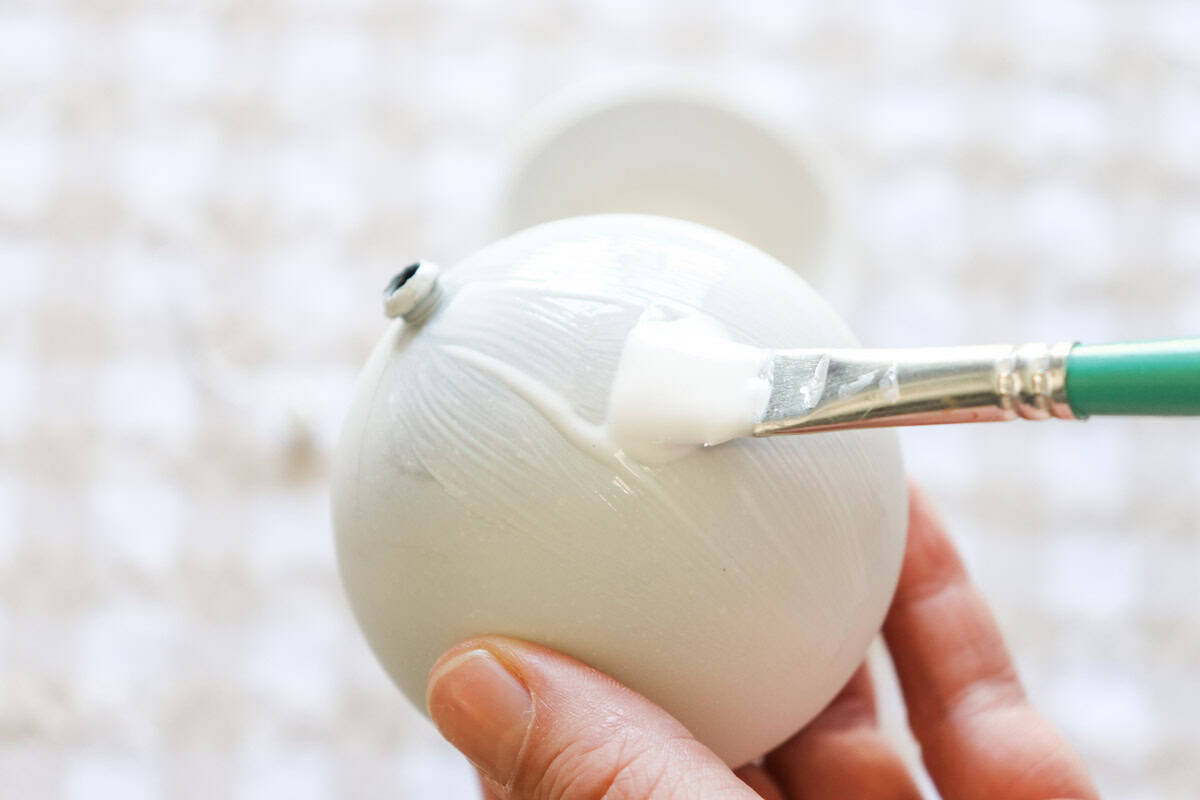 Applying Mod Podge glue to the bauble with a paintbrush