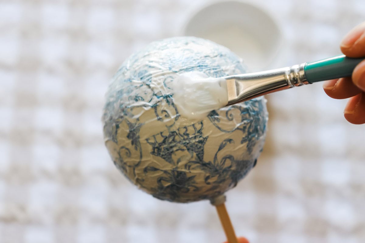 A final layer of glue is applied over the top of the decoupage bauble to seal it