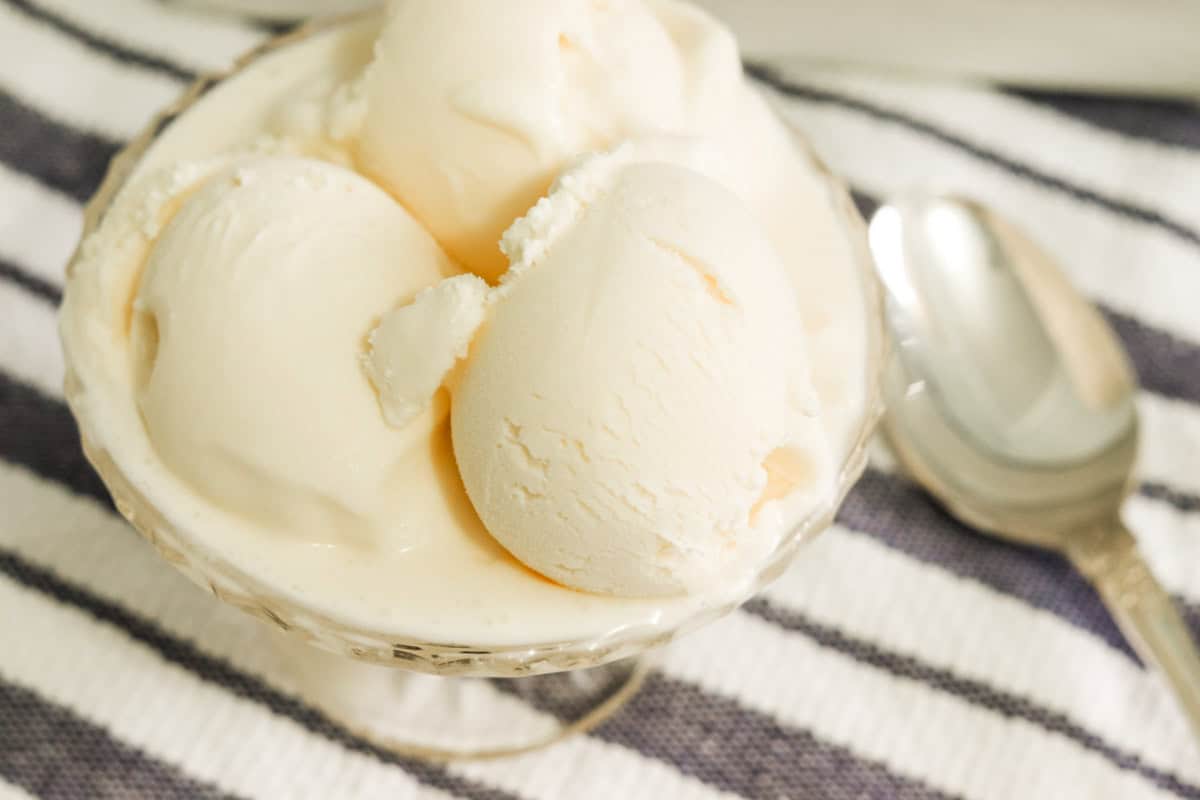 A close up image of scoops of home made ice cream with sweetened condensed milk in a bowl next to a spoon