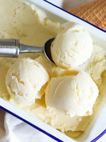 Custard base vanilla ice cream in a tin with an ice cream scoop