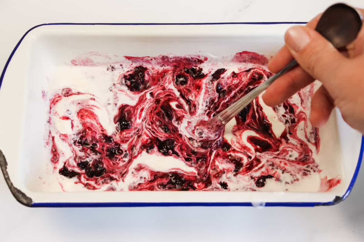 The berry sauce is swirled through the first layer of ice cream with the narrow end of a spoon