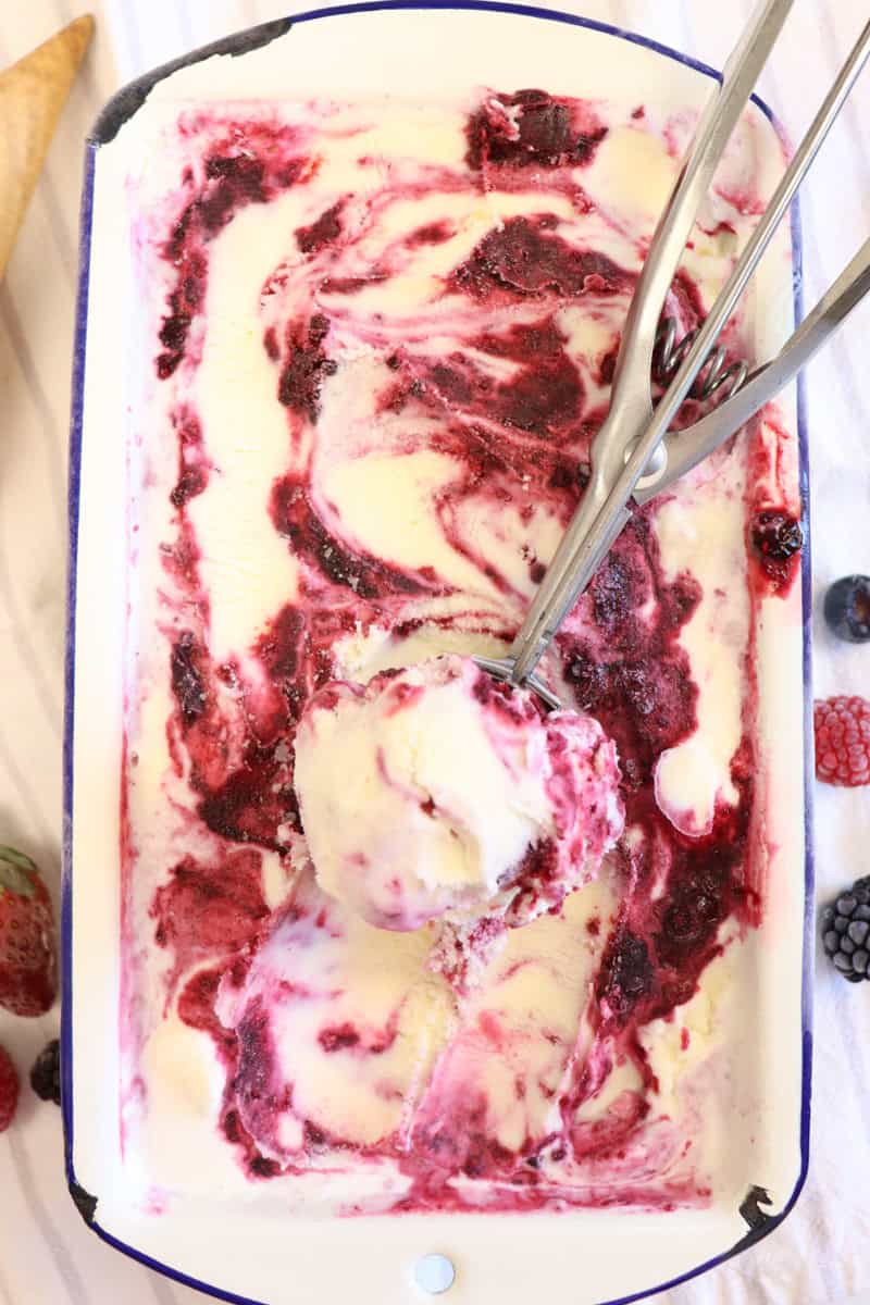 homemade berry ice cream being scooped out of the container surrounded by berries and waffle cones