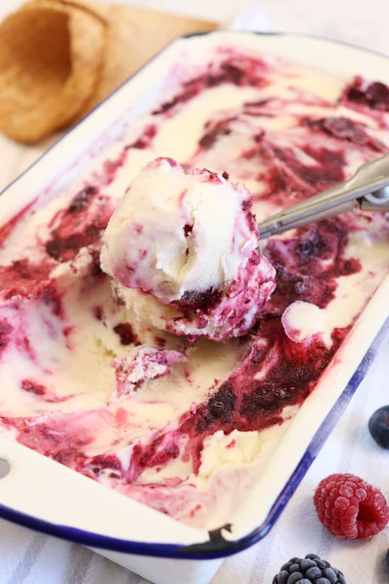 homemade berry ice cream being scooped out of the container surrounded by berries and waffle cones