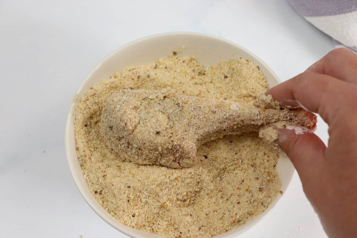 The lamb cutlet is dipped in a dish of bread crumbs
