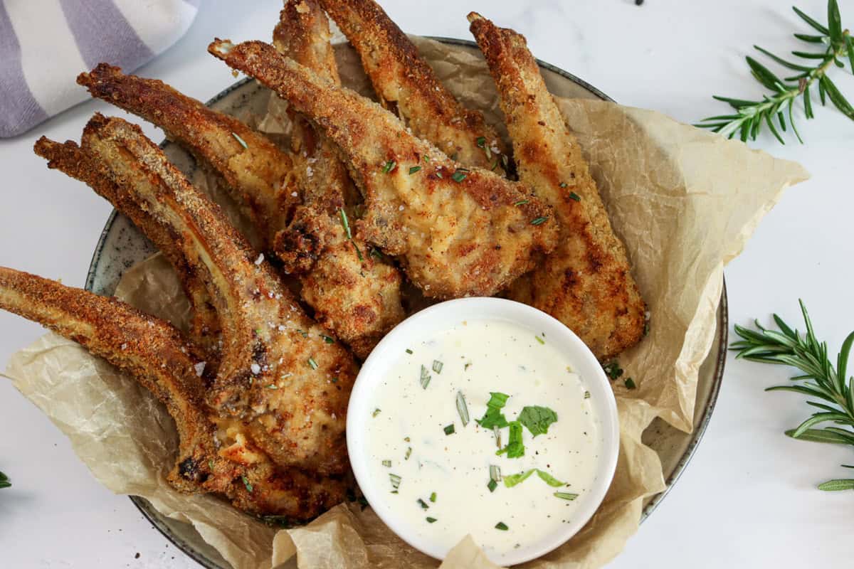 Crumbed lamb cutlets are served in a bowl with a bowl of dipping sauce