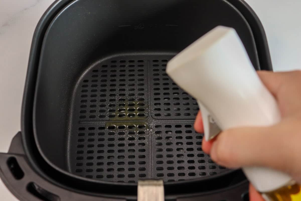 The air fryer basket is sprayed with extra virgin olive oil before the lamb cutlets are added