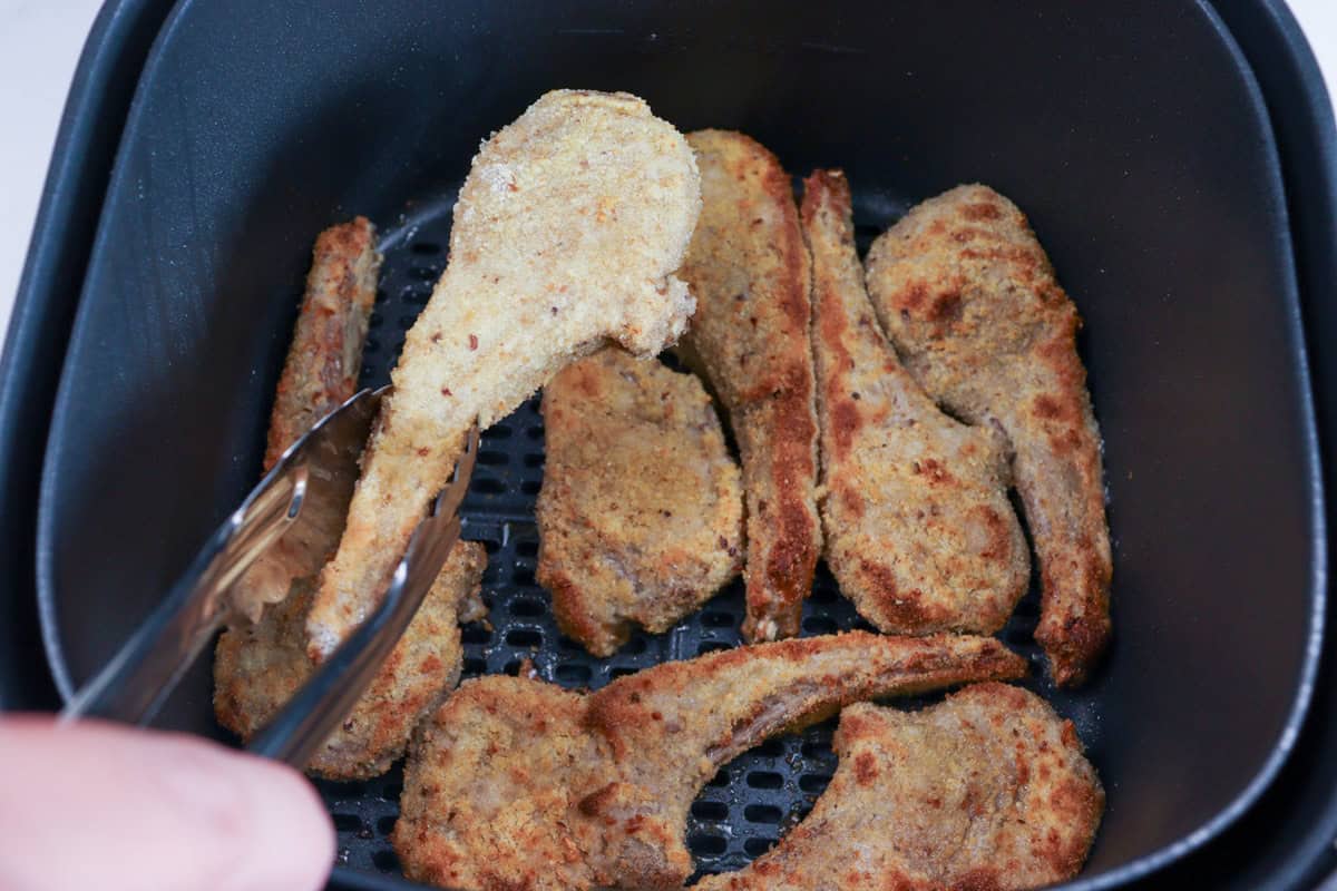 The lamb cutlets are turned in the air fryer basket half way through cooking using a pair of tongs