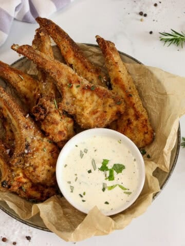 Crumbed lamb cutlets served in a bowl with a small bowl of sauce