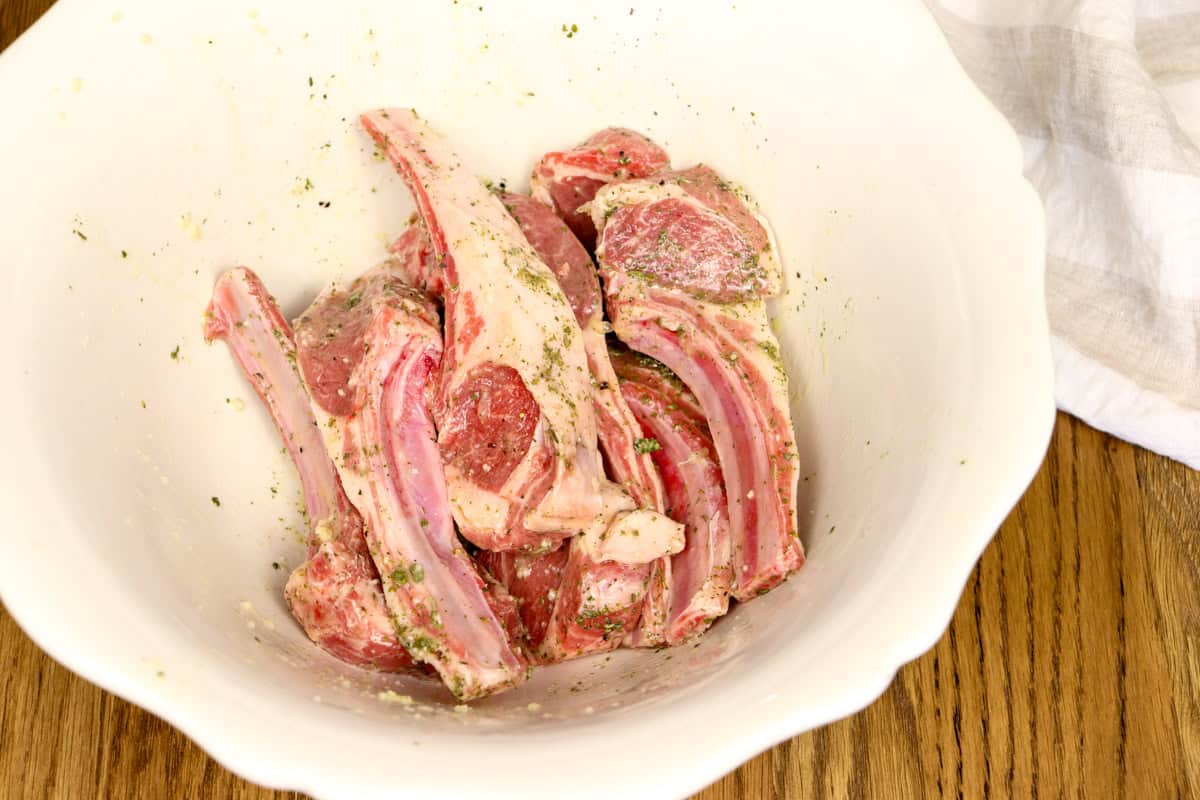 The lamb cutlets are marinating in olive oil, garlic, lemon juice, dried oregano, salt and pepper in a mixing bowl