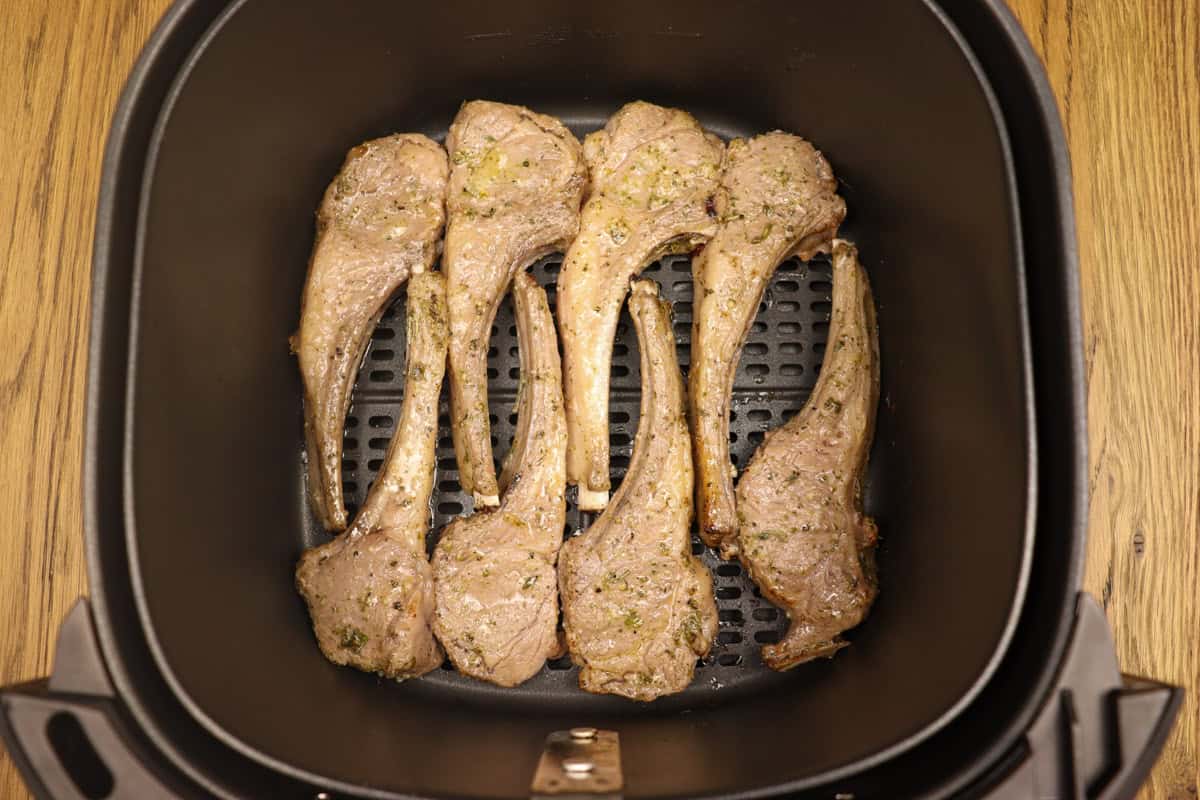 The lamb cutlets in the air fryer basket have been turned half way through the cooking time
