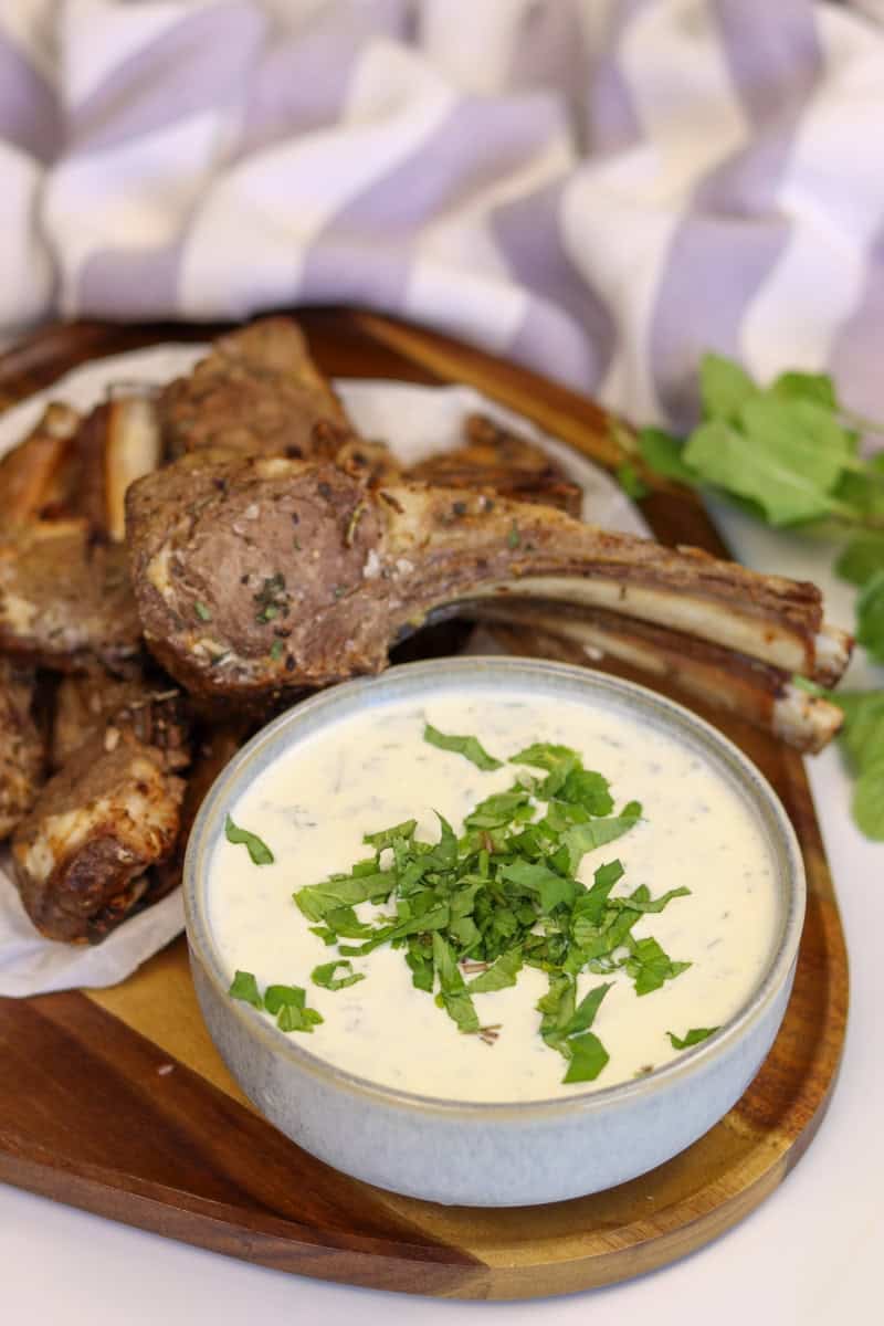 Yogurt and mint sauce served in a bowl on a platter with lamb cutlets