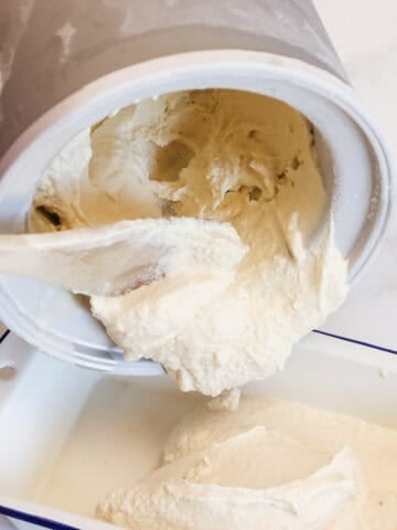 Freshly churned ice cream is being spooned out of the freezer bowl of an ice cream maker